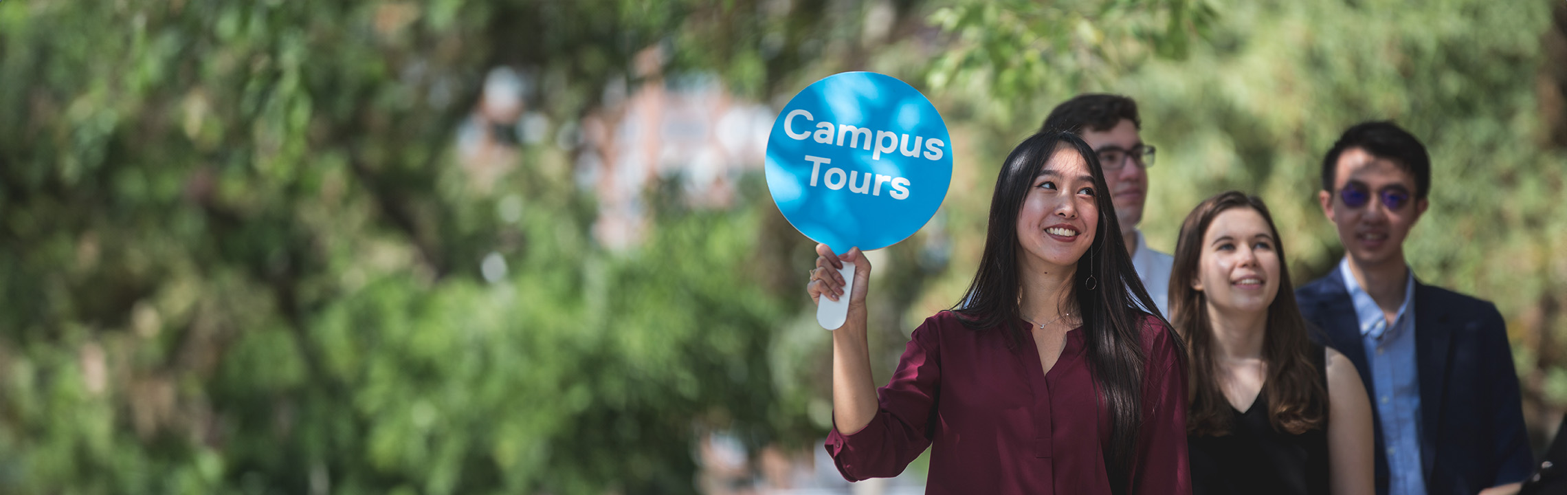 Guests following the campus tour guide with a sign in their hand.